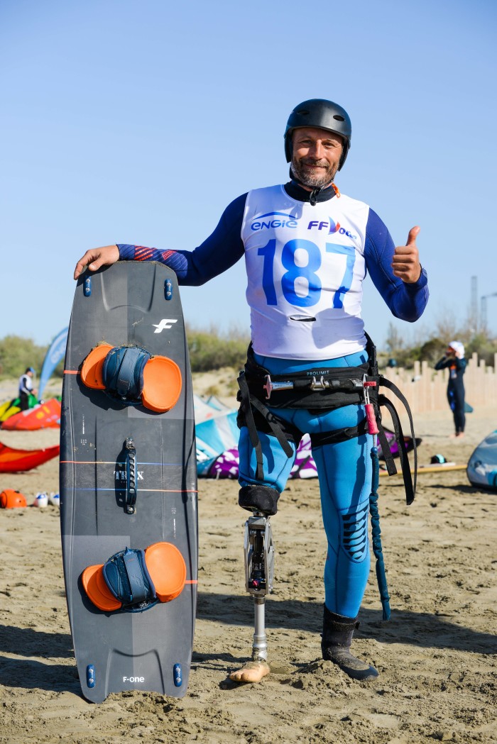 Un pratiquant de kitesurf avec une prothèse de jambe se tient sur la plage prêt à partir naviguer